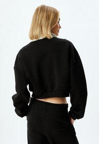 Suéter negro corto con corte holgado, cuello redondo y hombros caídos; combinado con pantalones joggers negros a juego; textura de tela suave.