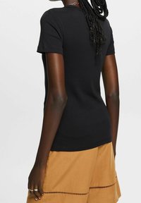Zwarte katoenen t-shirt met korte mouwen, ronde halslijn en een slim fit, gecombineerd met ontspannen beige shorts met een horizontaal patroon.