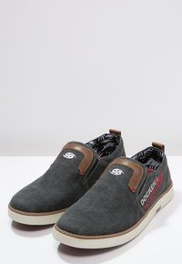 Chaussures slip-on en toile grise avec des accents en cuir brun, un logo blanc et une doublure intérieure à motifs. Elles présentent une surface texturée et une semelle en caoutchouc.