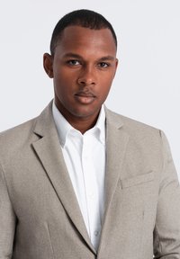 Blazer gris clair en tissu texturé, doté d'une poche poitrine simple, de revers crantés, associé à une chemise blanche à boutons bien taillée.