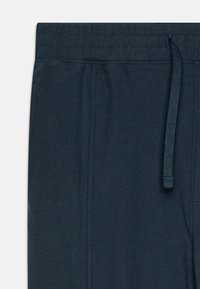 Námornícke modré jogger nohavice s elastickým pásom, sťahovacou šnúrkou a bočnými vreckami; vyrobené z mäkkej látky s hladkým povrchom.
