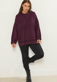 Un pull violet en tricot surdimensionné avec une texture côtelée et des accents de couture noirs, associé à un pantalon slim noir et des bottines.