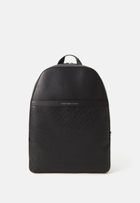 Sac à dos noir Tommy Hilfiger avec un motif monogramme en relief et une poignée supérieure, présenté sur un fond blanc.