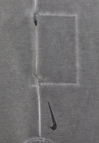 Szara bluza z kapturem z kieszenią na zamek, teksturowaną tkaniną i czarnym logo Nike na dolnej prawej stronie. Prosty design i funkcjonalne detale.