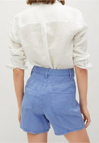 Jasnoniebieskie dżinsowe szorty z wysokim stanem, dwoma tylnymi kieszeniami i gładką fakturą. Połączone z białą lnianą koszulą, z podwiniętymi rękawami.