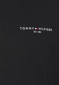 Svart bomull t-shirt med vit logotyptext "TOMMY HILFIGER EST. 1985" med röda och blå accentstripes på bröstet. Slät textur.