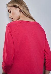 Jasnoróżowa, długorękawowa bluzka z szerokim dekoltem i podwiniętymi rękawami, charakteryzująca się miękką teksturą i lekko swobodnym stylem.