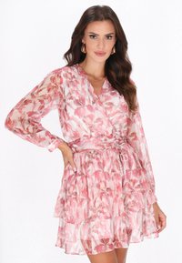 Vestido con estampado floral en tonos rosas, de manga larga, escote en forma de V y falda de volantes en capas. Confeccionado en una tela ligera y transparente, con lazo en la cintura.