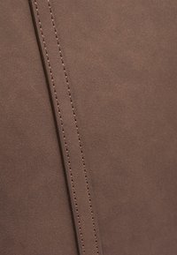 Tessuto scamosciato marrone con una superficie liscia, con cuciture visibili lungo una cucitura, che enfatizzano un design pulito e minimalista.