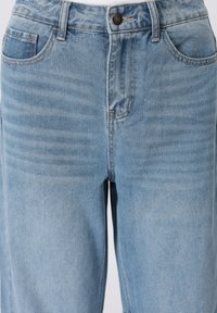 Φωτεινό μπλε τζιν με ευθύ σχεδιασμό παντελονιού, τυπικό στιλ με πέντε τσέπες και ορατές ραφές κοντά στη μέση.