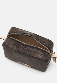 Borsa cosmetica marrone Calvin Klein con logo dorato, materiale texture, chiusura a doppia zip e motivo monogram CK su tutta la superficie.