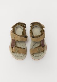 Bruna mockaskinnsandaler med grå gummisula, justerbara remmar, texturerad fotbädd och gummiyttersula, med en dämpad design för komfort.