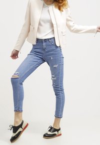 Světle růžová zkrácená bunda, bílý top, roztrhané modré skinny džíny s dírami a černobílé šněrovací boty s červenou podešví.