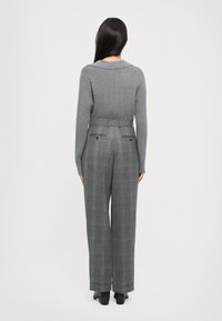 Harmaa ribattua neulepaita, jossa on leveä kaulus, yhdistettynä korkeavyötäröisiin ruudullisiin housuihin, joissa on sinisiä ja oransseja viivoja sekä takataskut.