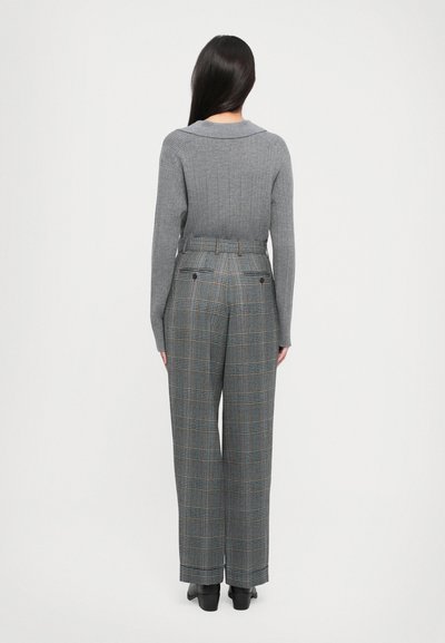 Szary sweter w prążki z szerokim kołnierzem, połączony z spodniami w kratę o wysokim stanie, z niebieskimi i pomarańczowymi liniami oraz tylnymi kieszeniami.