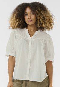 Camicia bianca button-up con maniche a sbuffo corte, realizzata in un tessuto leggero e con scollatura a V. Texture morbida con un sottile dettaglio di arricciatura sul davanti.