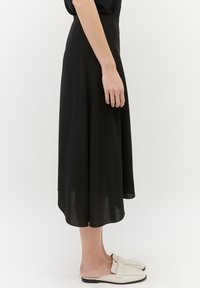 Sort midi-nederdel lavet af let stof, med en glat tekstur og en let udvidet design, parret med hvide slips-on sko.