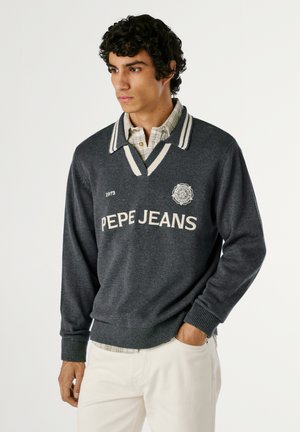Pull gris avec des accents de rayures blanches, présentant un col en V et le logo "PEPE JEANS". Porté par-dessus une chemise à carreaux. Texture douce, poignets côtelés.