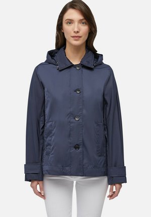 Giacca impermeabile blu navy con cappuccio, bottoni frontali e due tasche laterali. Presenta una vestibilità rilassata e un tessuto liscio e testurizzato.