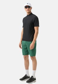Černé polo tričko, zelené šortky, černé sportovní boty, bílé ponožky, bílá kšiltovka s logem, černé sluneční brýle. Jednoduchý sportovní outfit.