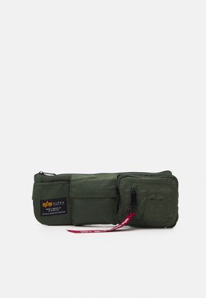 Ciemnozielona saszetka na pas z trzema kieszeniami na zamek i patkę, jedna z naszywką z logo Alpha Industries i czerwonym materiałowym uchwytem zamka.