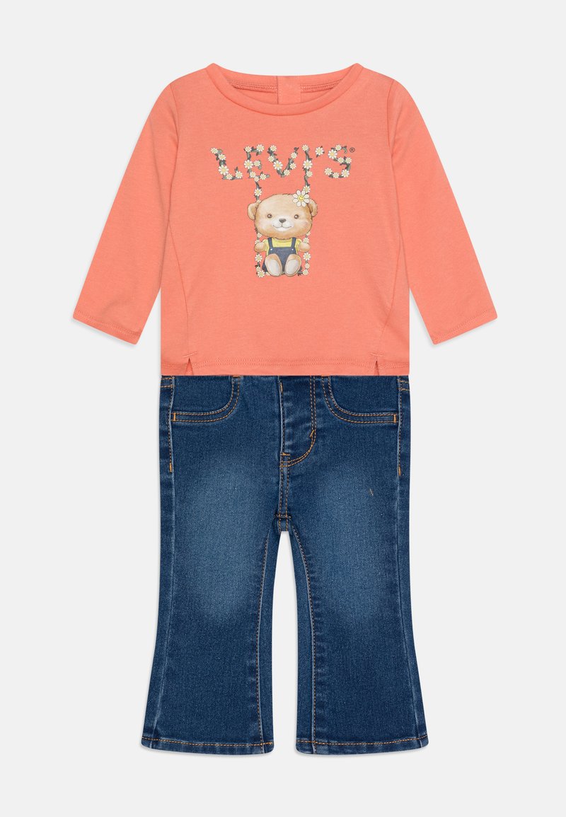 Top a maniche lunghe corallo con grafica di un orso e dettagli floreali, abbinato a pantaloni svasati in denim blu scuro con design classico a cinque tasche.