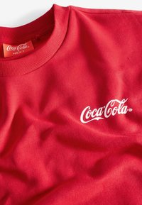 Rode katoenen T-shirt met een ronde halslijn en ribgebreide kraag, voorzien van een wit Coca-Cola logo dat op de voorkant is gedrukt. Soepele textuur.