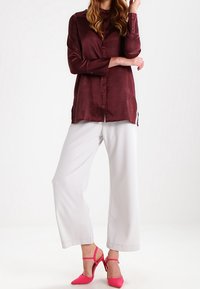 Bordeauxfärgad satinblus med långa ärmar och knäppning vid ärmsluten, tillsammans med lösa vita byxor. Rosa klackar med ankelsnören.