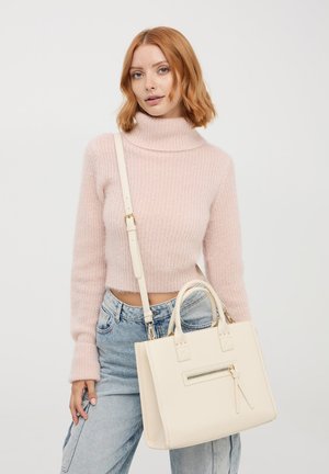 Borsa a mano in pelle beige con manici corti e tracolla regolabile, dotata di una tasca con zip frontale e corpo quadrato. Maglione colorato lavorato a maglia.