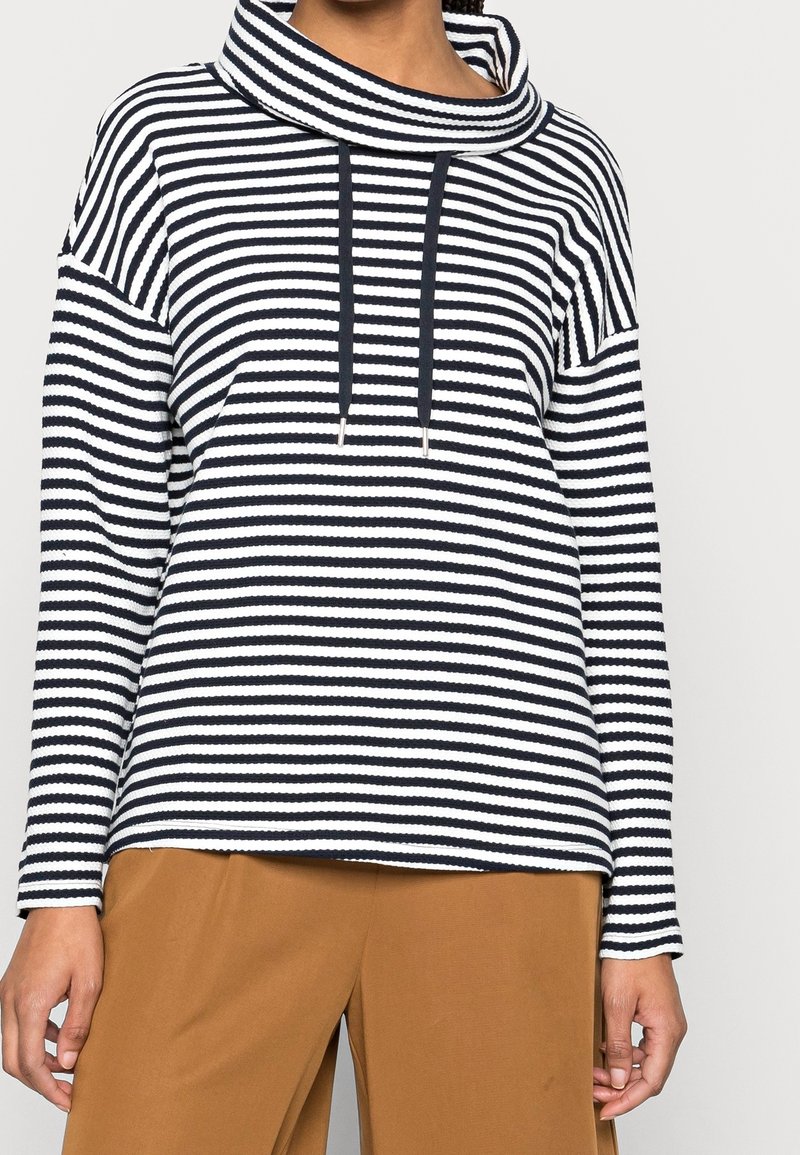 Proužkované tričko s rolákovým výstřihem v námořnické modré a bílé barvě, s volným střihem, dlouhými rukávy a šňůrkami jako detaily. Měkká texturovaná látka.