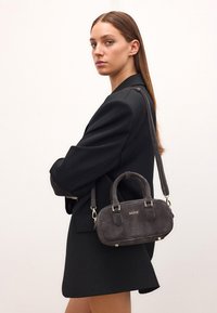 Grijze suede handtas met kleine dubbele handgrepen en een afneembare schouderband. Heeft gouden hardware en een rechthoekige vorm. Merkenlogo prominent weergegeven.