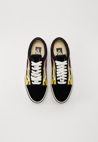 Paire de baskets Vans noires avec lacets blancs et bandes latérales, présentant des motifs de flammes rouges et jaunes sur les côtés, vues de dessus.