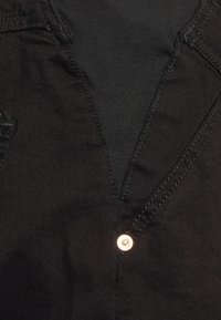 Top de denim preto com decote em V e uma ligeira textura. Apresenta um detalhe de botão com acabamento metálico e costura em contraste.