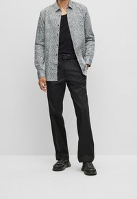 Camisa de manga larga con estampado en blanco y negro, con cuello abotonado, combinada con pantalones negros y zapatillas deportivas, con una textura suave.