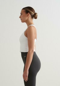 Valkoinen ribattu lyhythihainen crop top, joka on yhdistetty korkeavyötäröiseen tummanharmaaseen ribattuun legginsiin, jossa on pystysuoria raitoja ja pieni logotunnistus.