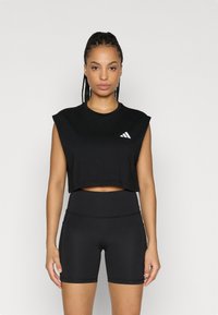 Μαύρο cropped αμάνικο τοπ από απαλό ύφασμα με στρογγυλή λαιμόκοψη και λευκό λογότυπο Adidas. Συνδυασμένο με ψηλόμεσο μαύρο σορτς.