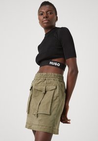 Fekete bordázott kantáros crop top rövid ujjakkal, amelyet egy olíva zöld cargo szoknyával párosítottak, oldalzsebekkel és rugalmas derékrésszel.