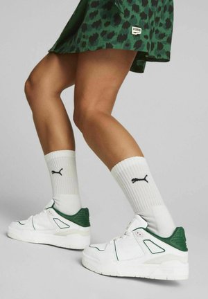 White sneakers with green accents, structured design, textured material, paired with white crew socks featuring a black logo.