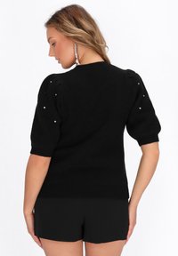 Suéter negro de punto con mangas cortas abullonadas, adornado con pequeños embellishments plateados en los hombros. Diseño limpio y acabado texturizado.