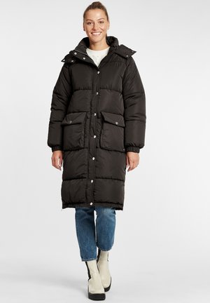 Svart pufferjakke med hette, trykknapper og to store frontlommer. Jakken er lett polstret og rekker til midten av leggen.
