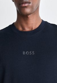 Námořnická modrá mikina vyrobená z bavlny. Vybavena žebrovaným výstřihem a vyvýšeným logem "BOSS" na hrudi. Hladká textura, volný střih.