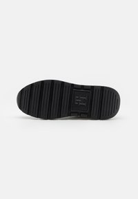 Schwarze Schuhsohle mit tiefen Profilen für Traktion, rechteckigem Logodetail, glatten Kanten und flacher Gesamform, ausgelegt für Stabilität.