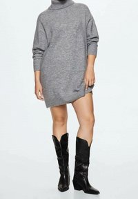 Szary sweterdzianinowy z wysokim kołnierzem, w oversize'owym fasonie i ściągaczami na mankietach. W zestawieniu z wysokimi czarnymi skórzanymi botkami z spiczastymi noskami.
