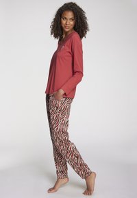 Langsleeve rood bovenstuk met een V-hals en hartdetail, gecombineerd met gestreepte broek in rood, wit en zwarte golvende lijnen.