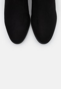 Botines negros de ante, con punta afilada y textura suave. Las suelas son planas y redondas, sin adornos visibles.