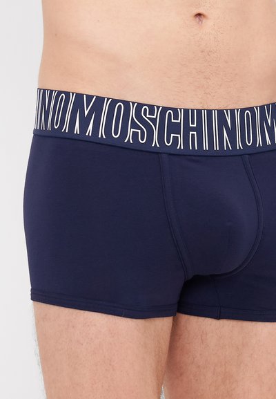 Námořnické modré boxerky vyrobené z jemné bavlny, s širokým páskem, na kterém je značkové jméno "Moschino" v bílých písmenech.