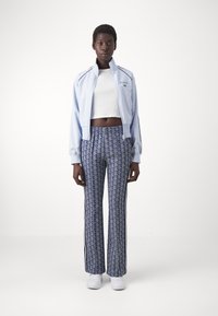 Light blue zip-up jacket with black accents, paired with patterned blue trousers featuring vertical stripes. Model wears white cropped top and sneakers.