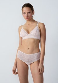 Bralette en dentelle rose clair avec des bords festonnés et une forme triangulaire, accompagnée de shorty en dentelle assortis présentant des motifs intricats.