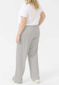 Un pantalon à jambes larges rayé en tissu noir et blanc présente une coupe décontractée et une texture douce, associé à un t-shirt blanc uni.