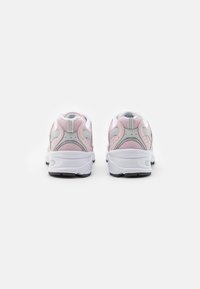 Ein Paar rosa und graue Mesh-Sneaker mit weißen dicken Sohlen, von hinten auf einem weißen Hintergrund abgebildet.